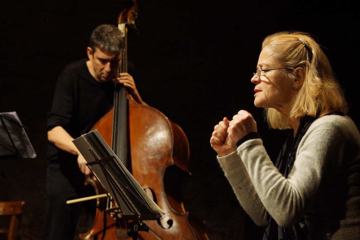 © Verena Buss Eine Frau sitzt vor einem Notenständer und liest davon ab, im Hintergrund spielt ein Mann Kontrabass